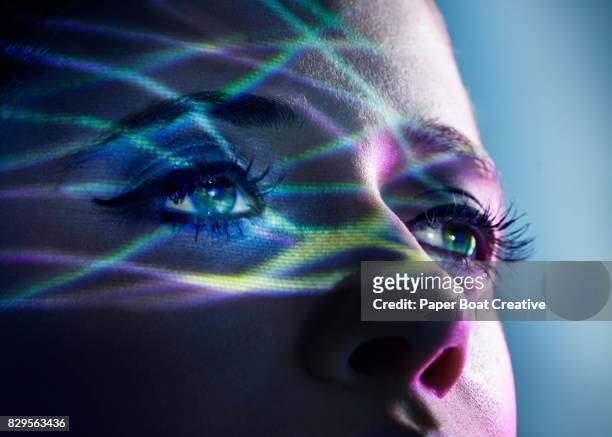 Thin light beams going across the eyes of a woman, shot against a blue studio background