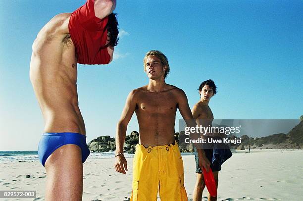 three young men wearing swimwear on beach - young men in speedos 個照片及圖片檔
