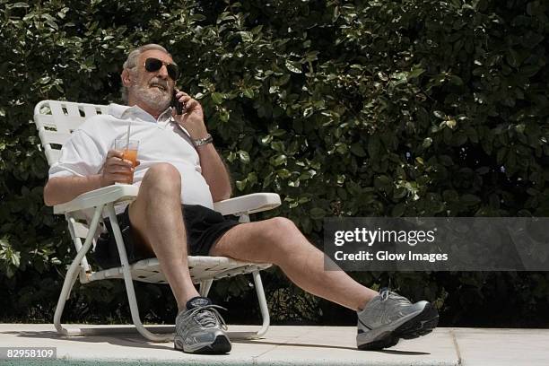 senior man sitting on a chair and talking on a mobile phone - folding chair stock-fotos und bilder