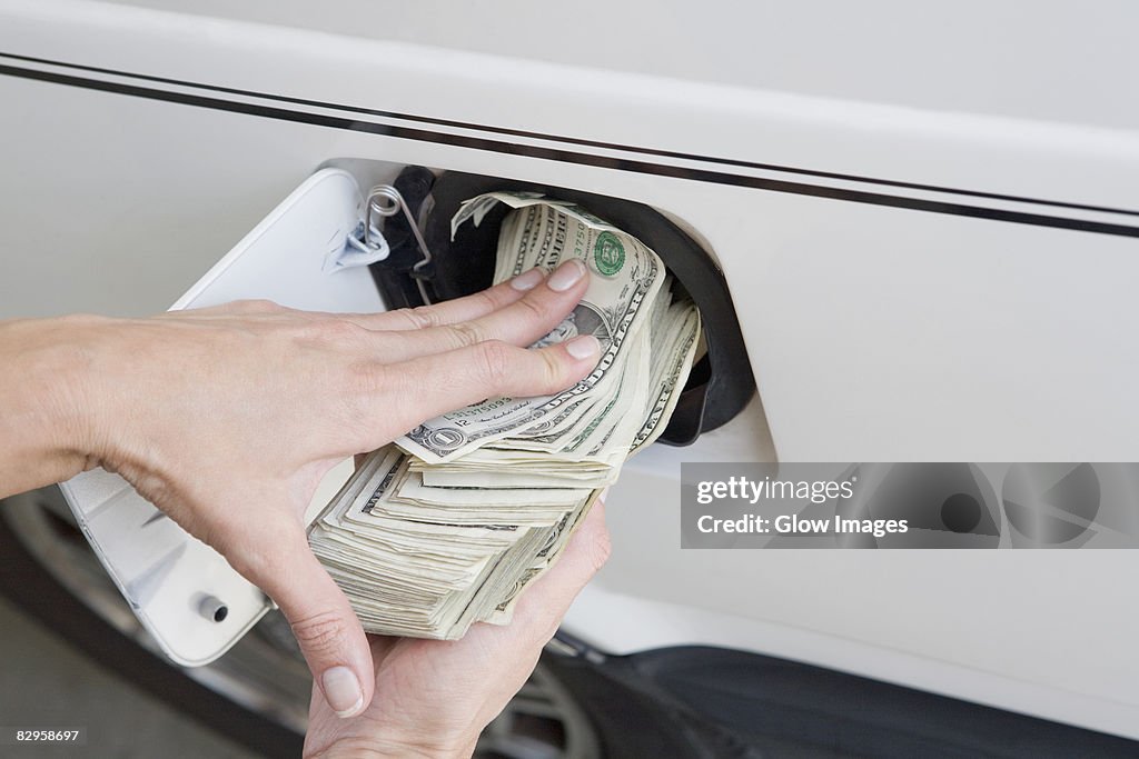 Close-up of a person's hands putting US paper currency in a gas tank of a car