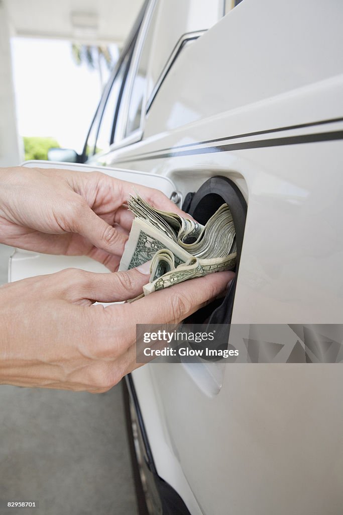 Close-up of a person's hands putting US paper currency in a gas tank of a car