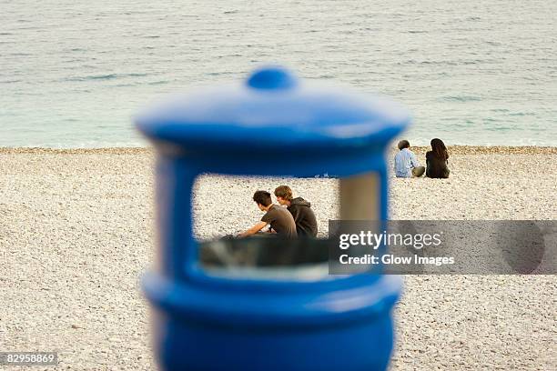 couple sitting on the beach viewed through a garbage bin, baie des anges, nice, provence-alpes-cote d'azur, france - france beach stock pictures, royalty-free photos & images