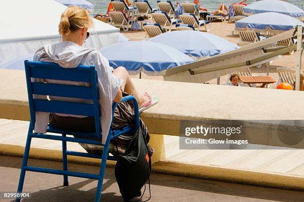 rear view of a woman sitting in an armchair on the beach, plage de la croisette, cote d'azur, cannes, provence-alpes-cote d'azur, france - parasol de plage fotografías e imágenes de stock