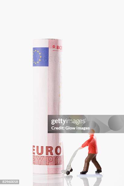 figurine of a manual worker carrying european union euro note on a push cart - fajo de billetes de euro fotografías e imágenes de stock