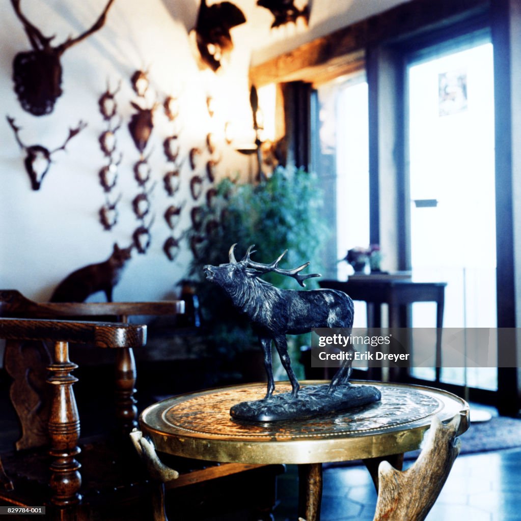 Statue of stag on table in room with animal head trophies