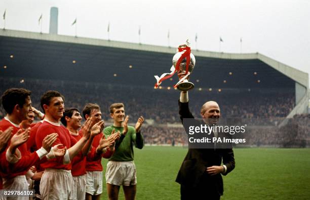 Manchester United manager Matt Busby holds the League Championship trophy aloft as his players applaud: Shay Brennan, Bill Foulkes, Tony Dunne, Pat...