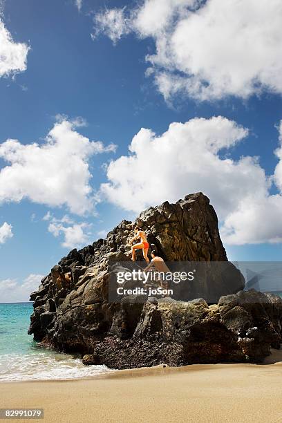 couple climbing rock at beach - waimea bay hawaii stock pictures, royalty-free photos & images