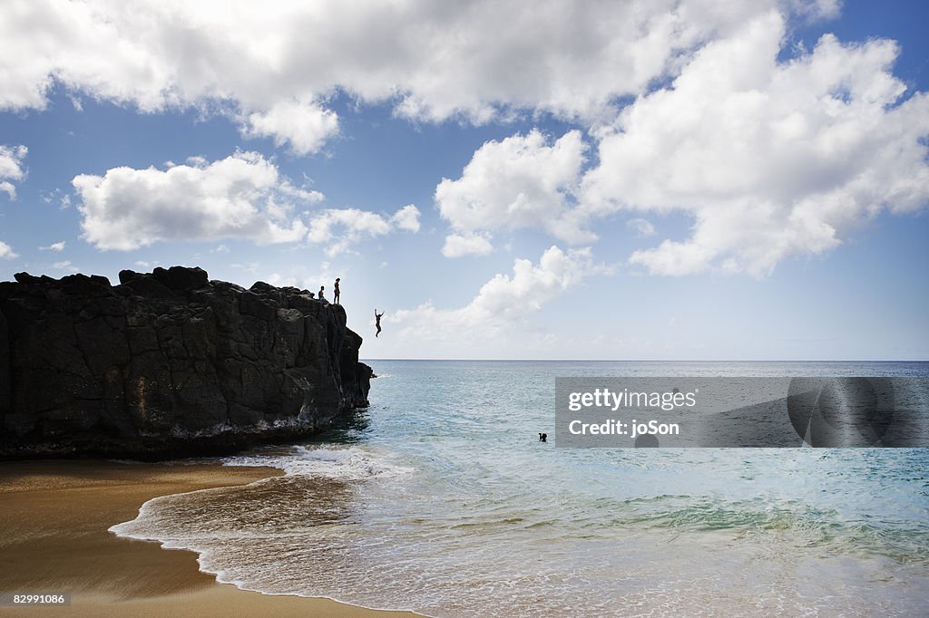 People standing on rock, woman jump into ocean