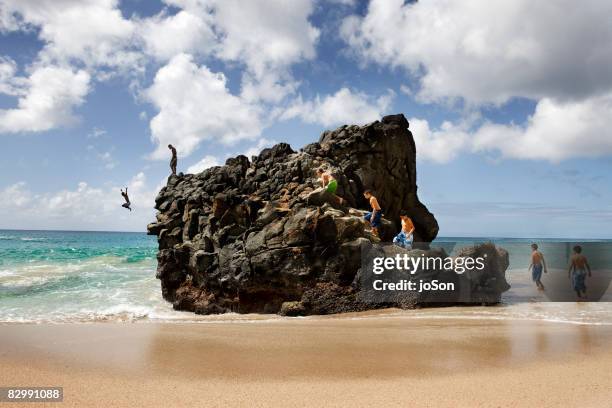 friends climbing and jumping off rock into ocean - waimea bay stock pictures, royalty-free photos & images