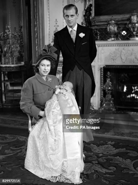 Princess Elizabeth holding Prince Charles in his Christening gown with her husband, the Duke of Edinburgh behind.