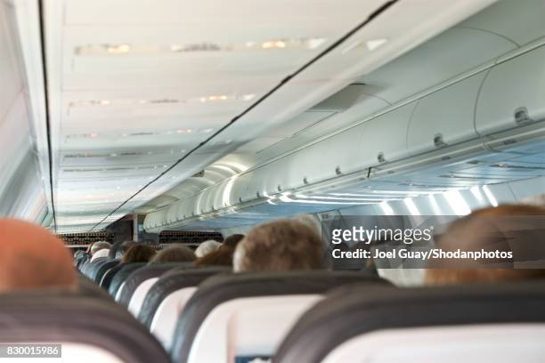 view from rear of loaded airplane looking forward across seat tops - luggage rack stock-fotos und bilder