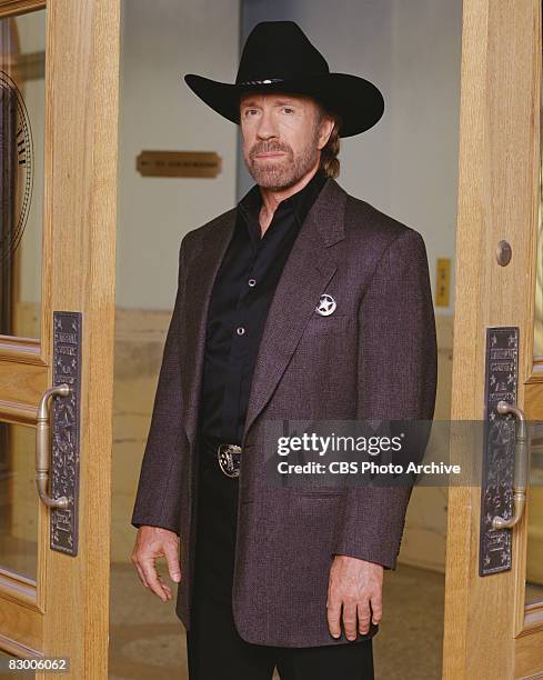 Promotional portrait of American actor Chuck Norris , dressed in a blazer over a black satin shirt and a black stetson, as he poses in a doorway for...