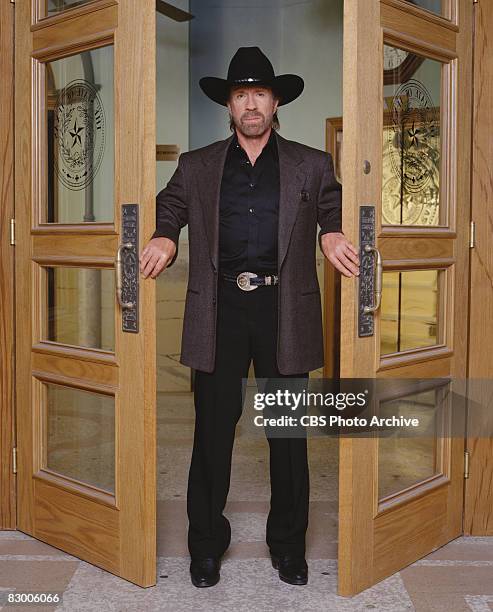 Promotional portrait of American actor Chuck Norris , dressed in a blazer over a black satin shirt and a black stetson, as he poses between two open...