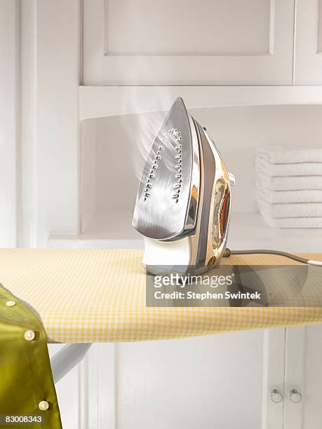 a steaming hot iron on a ironing board  - iron appliance stock pictures, royalty-free photos & images