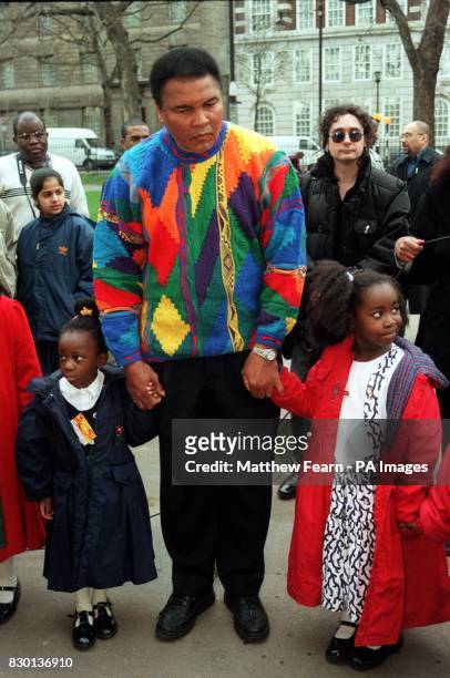 Boxing legend Muhammad Ali holds hands with some children before he lays a wreath at a monument in London as part of a campaign by the Jubilee 2000...
