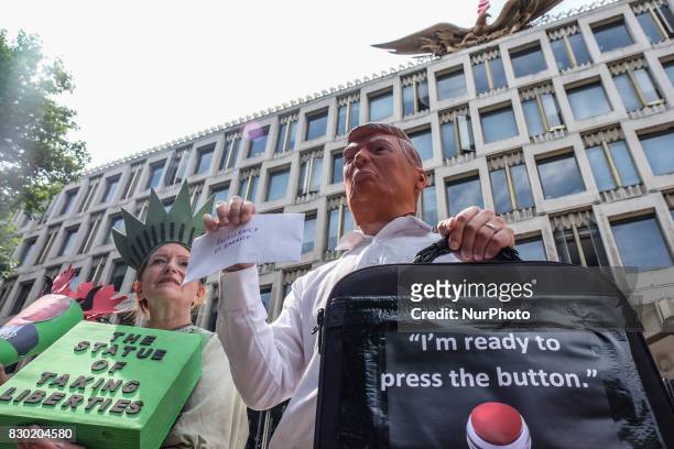 Man wearing a Donald Trump mask holds up a bag with a sign saying 'redy to push the button' and a woman dressed as 'The Statue of Taking Liberties'...