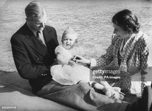 Prince Charles, later The Prince of Wales, perched on the lap of his father the Duke of Edinburgh, whilst his mother Queen Elizabeth II looks on in...