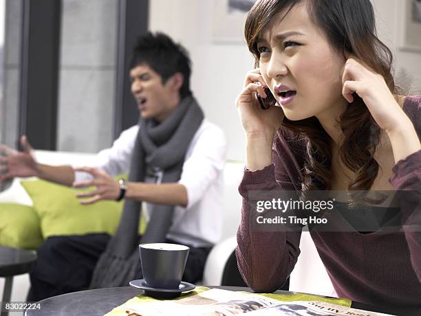 woman on cell phone, man yelling in background - fingers in ears stock pictures, royalty-free photos & images