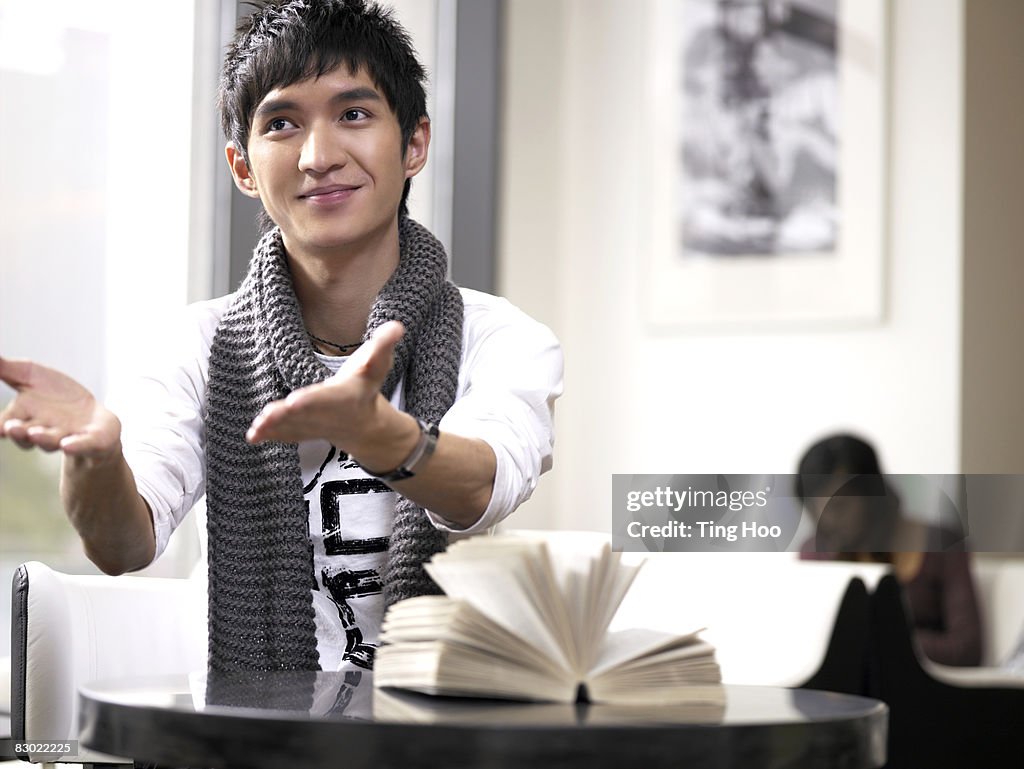 Man with book sitting in cafe, arms outstretched