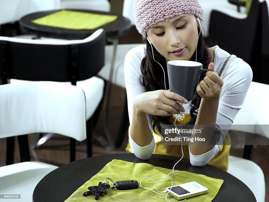 Woman with coffee listening to MP3 player in cafe