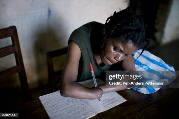 Woman writes notes in a book in her small house in Bukavu, DRC. She was abducted, held captive and raped by rebels in the DRC conflict. Her hands...