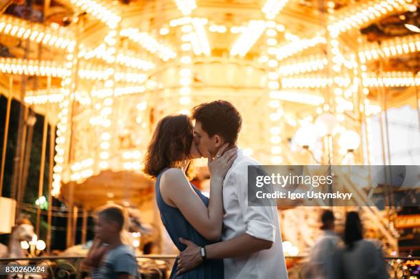 couple kissing near the marry-go-round in the park - der kuss stock-fotos und bilder