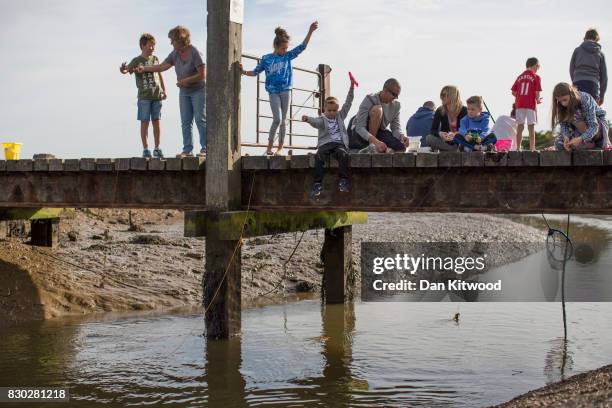 Holiday makers sit on a wooden bridge while fishing for crabs on August 11, 2017 in Walberswick, England. Much of the country is expected to enjoy a...