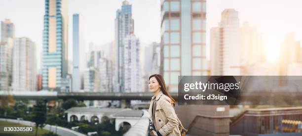 confident corporate woman overlooking the cityscape of hong kong on urban balcony - asian woman smiling sunrise stock pictures, royalty-free photos & images