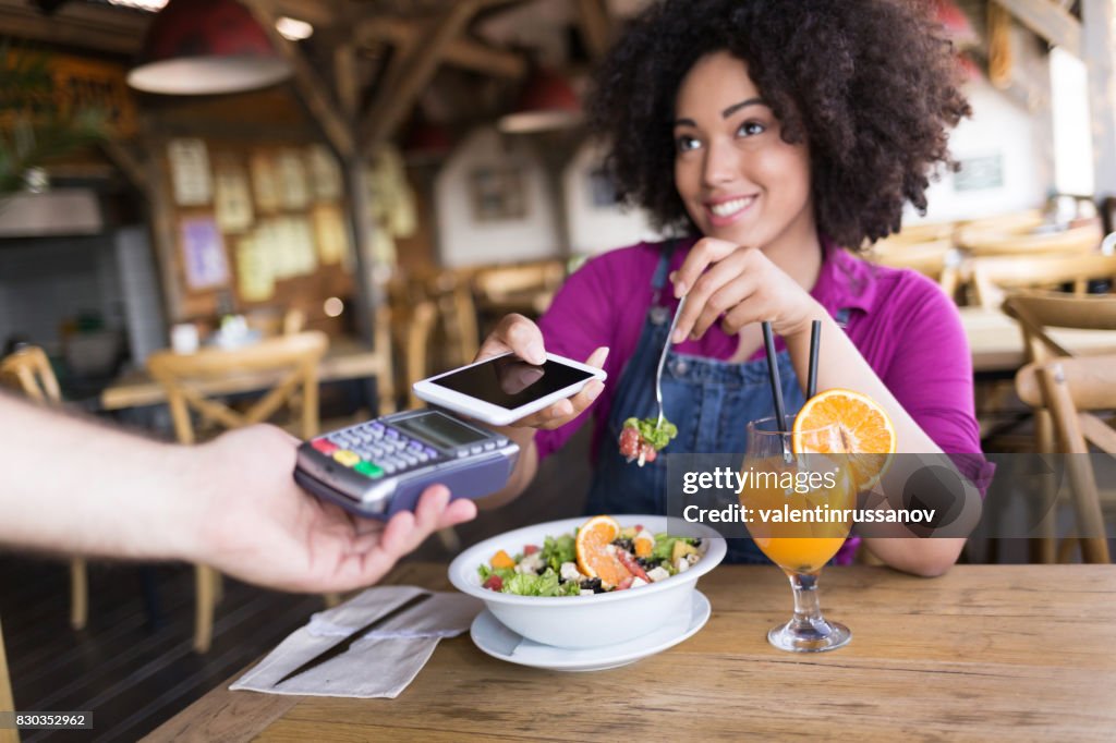 Leende kvinna använder mobil betalning i restaurang