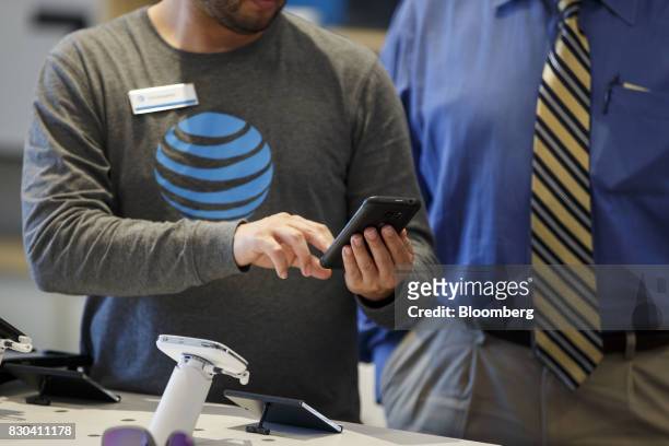 An employee helps a customer with a smartphone at an AT&T Inc. Store in Newport Beach, California, U.S., on Thursday, Aug. 10, 2017. AT&T Inc. Shares...