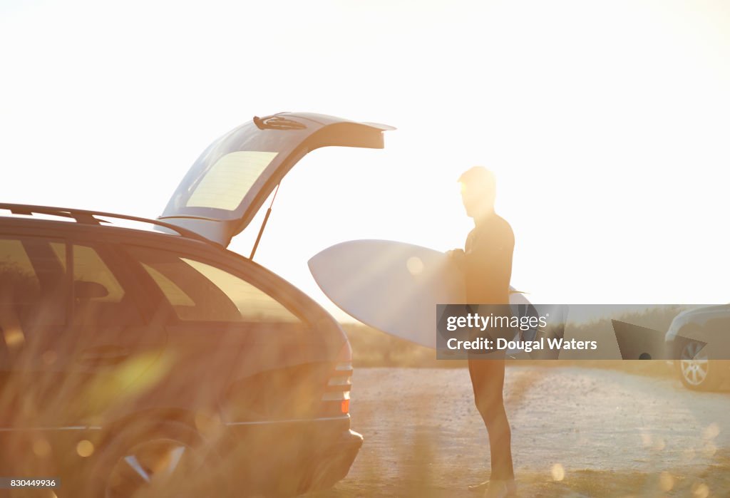 Surfer taking surfboard out of car.