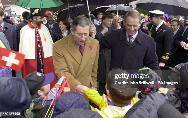 The Prince of Wales shakes hands with school children, while President Ogi of Switzerland holds an umberella over his head. The Prince was on a...