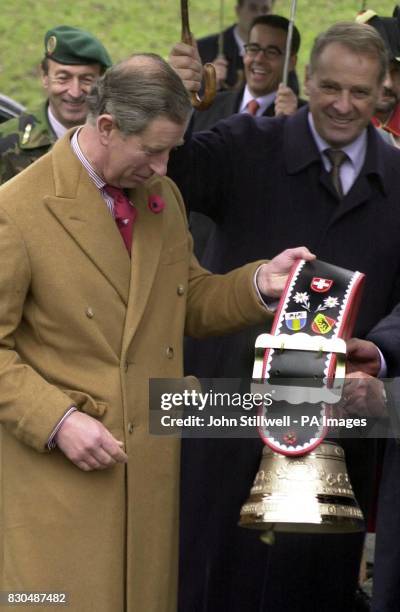 The Prince of Wales gets a giant alpine cow bell as a gift, while President Ogi of Switzerland holds an umberella over his head. The Prince was on a...