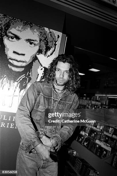 Australian singer songwriter Michael Hutchence of the rock band INXS, poses for a photo in front of a poster of Jimi Hendrix while shopping for CDs...