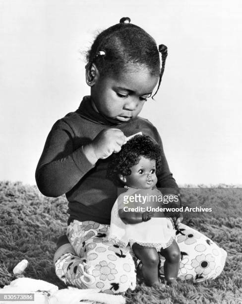 Young girl brushing the hair of her new Shindana Kimmie doll, Los Angeles, California, 1974.