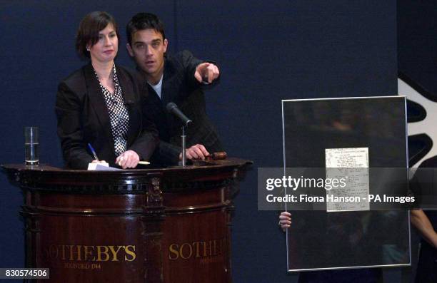 Singer Robbie Williams joins auctioneer Kerry Taylor as she auctions the singers hand-written lyrics to the hit single 'Angels', which sold for...