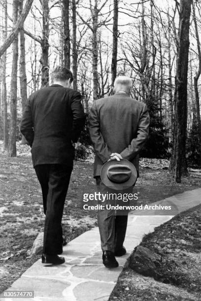 President John F Kennedy walks along a stone pathway with former President Dwight Eisenhower while contemplating the issue of the Bay of Pigs...