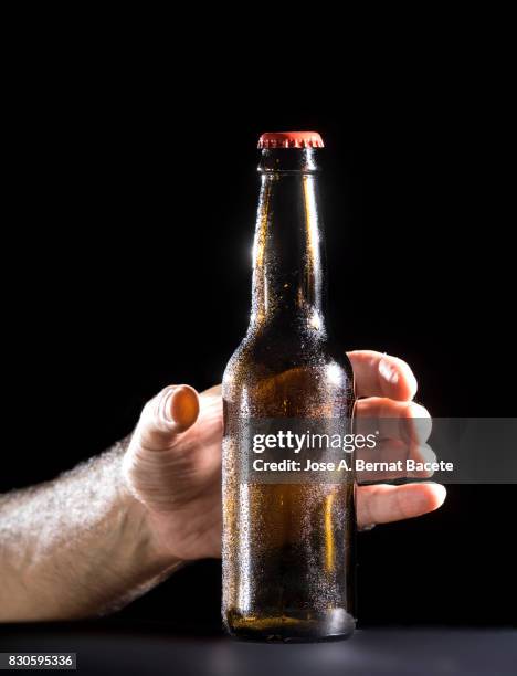 bottle of beer with the glass esmerilado with drops of water and the hands of a man grab  on a black background - beer mat stockfoto's en -beelden