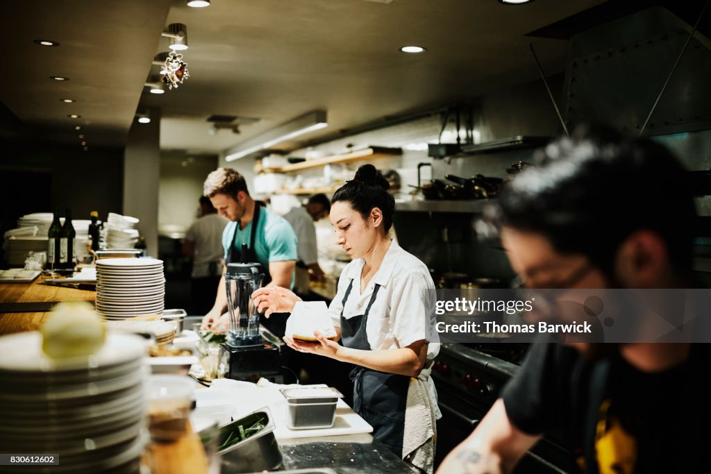 Female chef working with block of Parmesan cheese while preparing for dinner service in restaurant kitchen