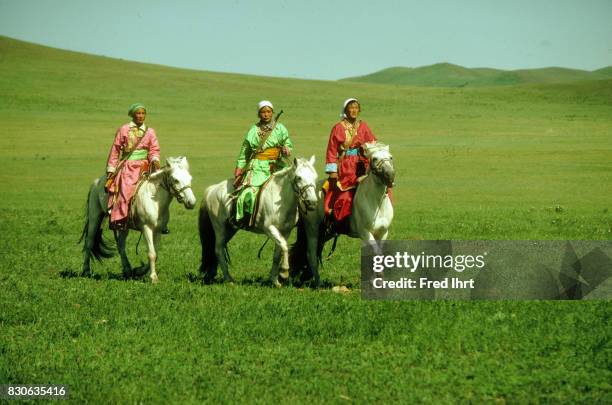 Three Mongolian Woman on horses dressed in the traditional deel. Rifles over their shoulders. They belong to the nomads police. The deel outfit is a...