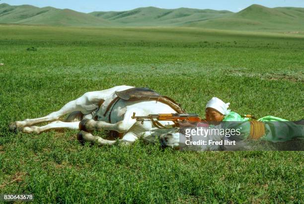 Mongolian nomadic woman with shouldered rifle laying down with her horse in the vast grassland. She belongs to the nomad police and wears the...