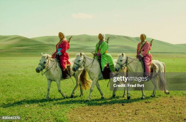 Three Mongolian Women on horses dressed in the traditional deel. Rifles over their shoulders. They belong to the nomads police. The deel outfit is a...