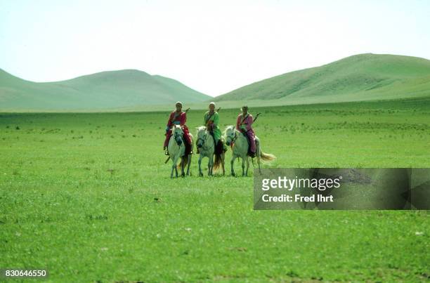 Three Mongolian women riding their horses in the grassland. Dressed in the traditional deel. Rifles over their shoulders. They belong to the nomads...