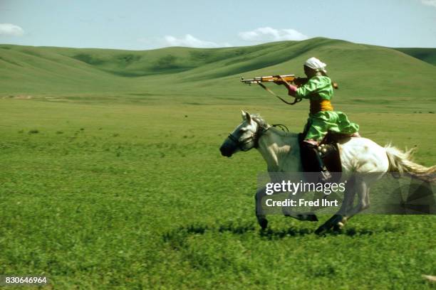 Mongolian nomad woman galloping on her horse practicing her rifle skills. She belongs to the nomads police. The deel outfit is a symbol of pride and...