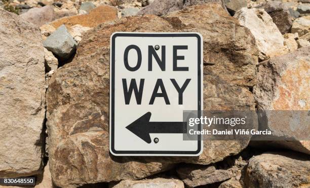 one way sign post pointing left over a stone background - einbahnstraßenschild stock-fotos und bilder