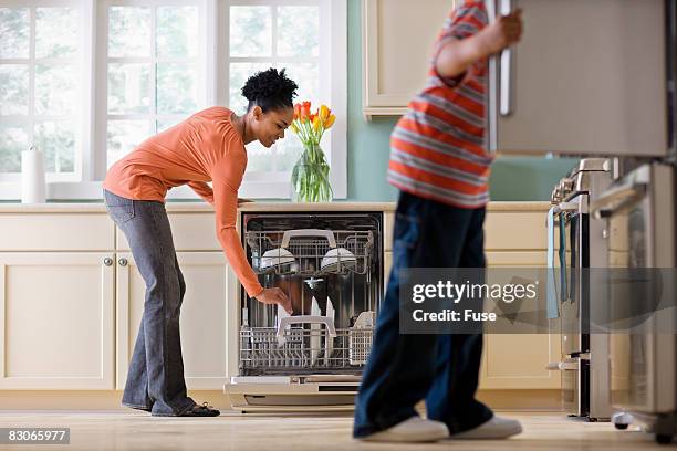 woman unloading dishwasher while son looks in refrigerator - loading dishwasher stock pictures, royalty-free photos & images