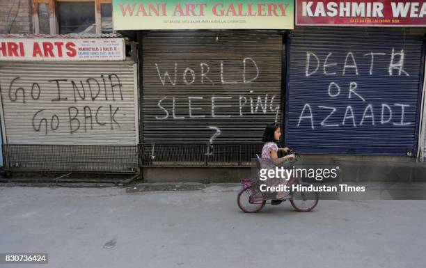 Kashmiri girl rides bicycle in front of closed shops during restrictions in a downtown area on August 11, 2017 in Srinagar, India. Authorities...