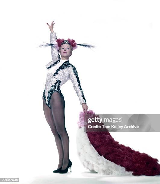 Portrait of American actress and dancer Eleanor Powell , in a customized matador's costume, raises her right arm high in the air and holds a red and...