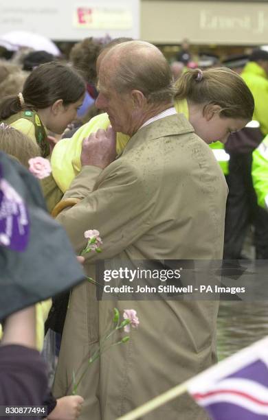 The Duke of Edinburgh lifts a young girl over the barrier so that she can give Queen Elizabeth II her flowers as she tours Leicester city centre, on...