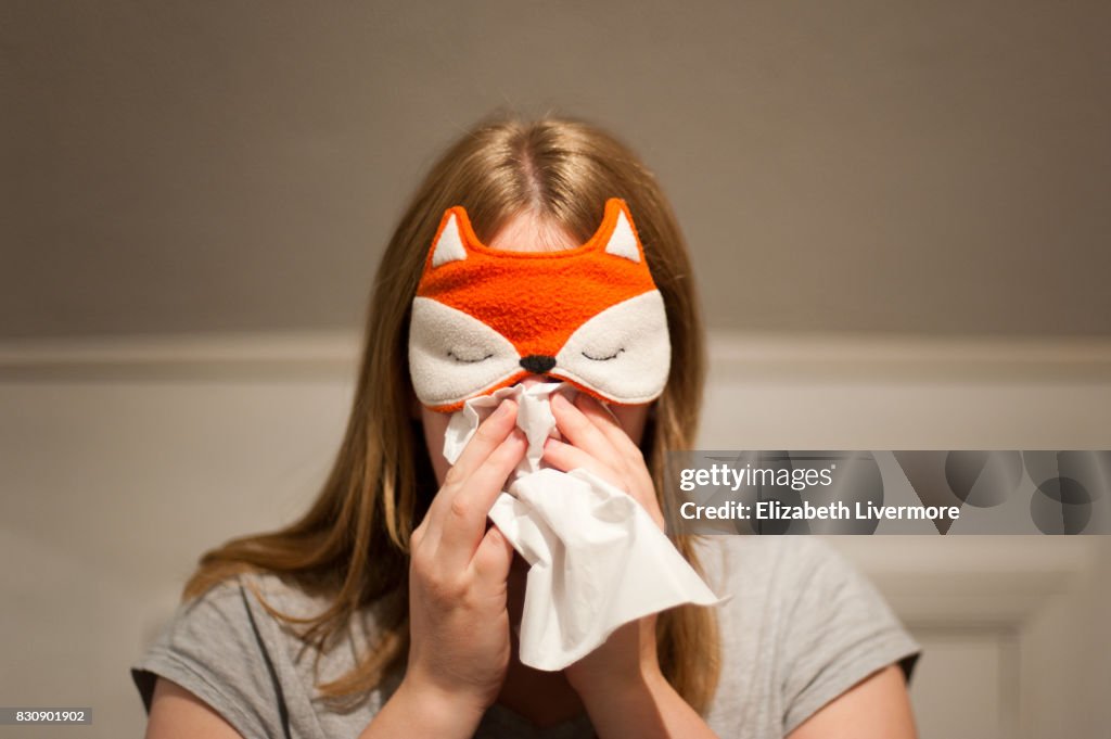 Woman wearing face mask, blows her nose with tissue